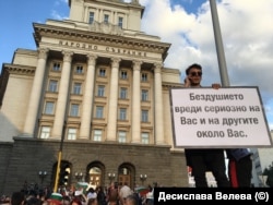 Млад мъж се е качил нависоко пред сградата на бившия Партиен дом с плакат "Бездушието вреди сериозно на Вас и на другите около Вас".