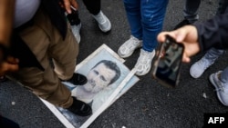 Демонстрант стоит на фотографии президента Башара Асада во время акции протеста у сирийского консульства в Стамбуле, 8 декабря 2024 года. 