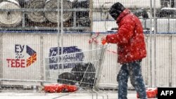 Мъж с количка с покупки минава през площад в Скопие на фона на надпис "ЕС за теб". 