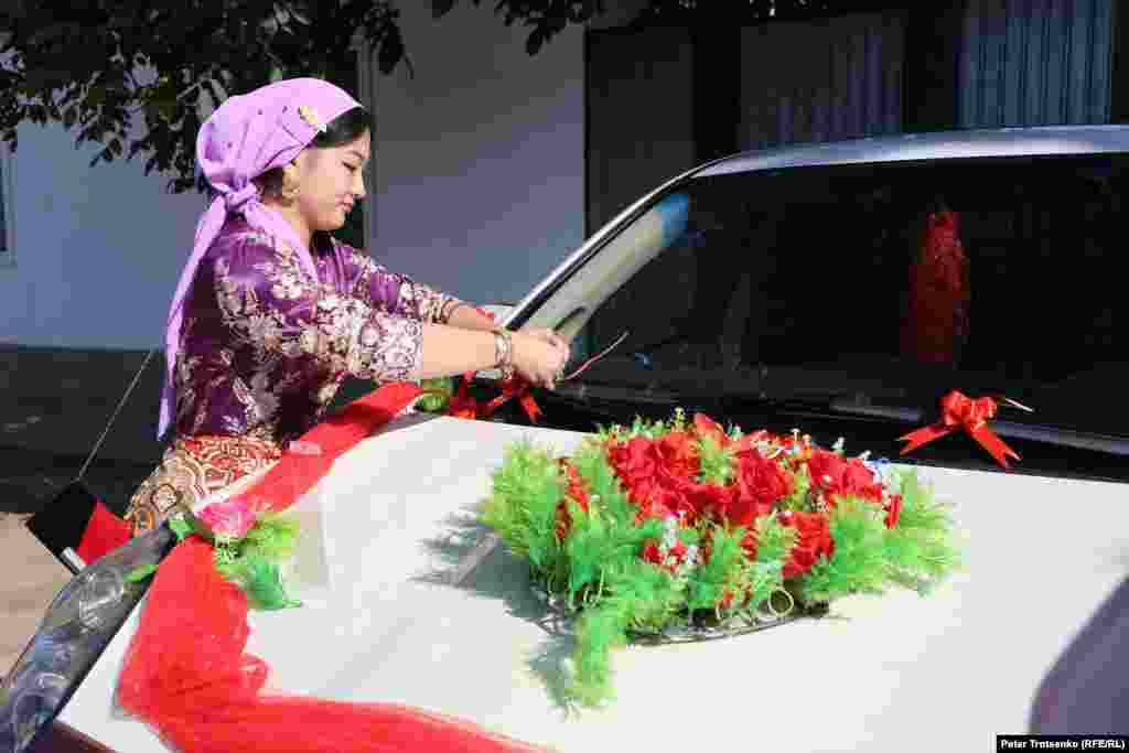 The groom&#39;s relatives are getting ready to pick up the bride. In this photo, a woman decorates the car in which Roza will be taken to the house of her future husband.