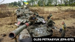 Ukrán katonák kezdenek megszerelni egy zsákmányolt, de sérült orosz tankot Harkiv közelében 2022. szeptember 15-én