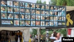 Двама души се прегръщат под банер със снимки на заложниците, поставен в Тел Авив. Снимката е от 9 октомври, когато стана известно, че е договорено връщането на израелските заложници срещу освобождаване на затворници от Хамас.