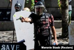 Alan Swinney rendőr fog fegyvert egy tüntetőre, miközben többek közt a Proud Boys és a Patriot Prayer csoportjai összecsapnak a rendőri erőszak és a faji diszkrimináció ellen tüntetőkkel 2020. augusztus 22-én az oregoni Portlandben.