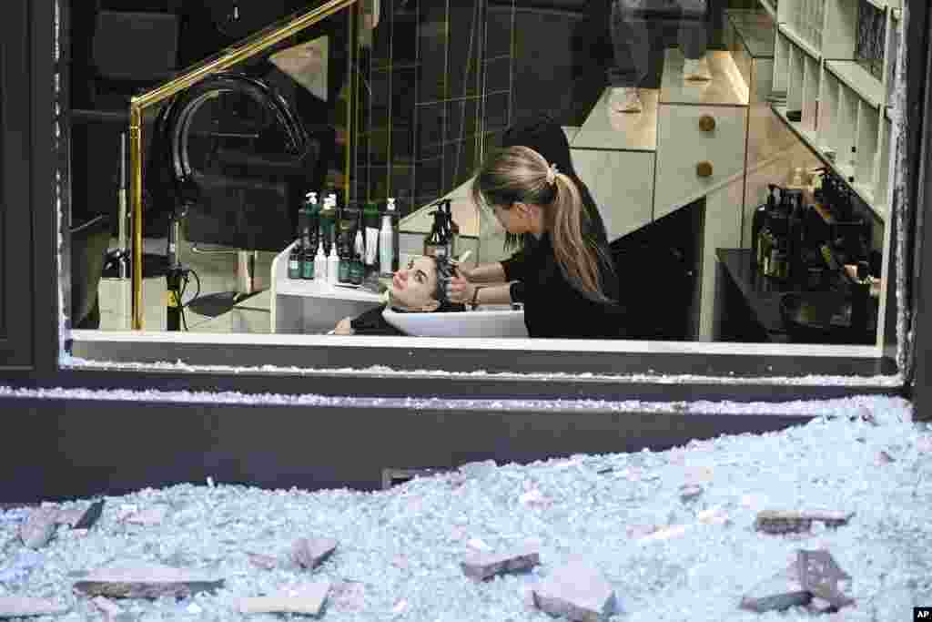 Груда осколков стекла из витрины магазина возле салона, где парикмахер укладывает волосы клиентке, после атаки БПЛА, Киев, Украина, 28 августа 2025 г. AP Photo/Danylo Antoniuk