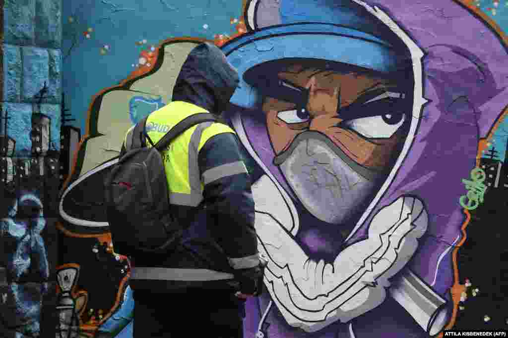 Велосипедист го турка својот велосипед покрај графит на кој се гледа лик со маска во Будимпешта, Унгарија.