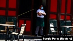 Madridban egy pincér áll maszkban egy étterem teraszán vendégre várva.