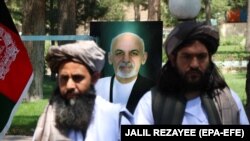 Taliban members stand in front of a portrait of Afghan President Ashraf Ghani as they attend a ceremony after being released in Herat on May 26.