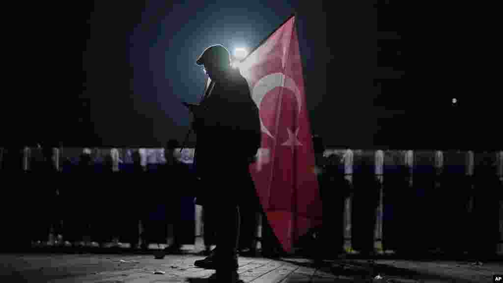 Egy tüntető török zászlóval március 23-án Isztambulban a rendőrsorfal és a bíróság épülete előtt
