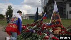 Orosz nemzeti zászlót viselő férfi térdel egy rögtönzött emlékmű előtt az egykori Wagner-központ közelében Szentpétervárott, Oroszországban 2023. augusztus 25-én