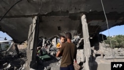 Palestinac drži dijete u naručju i posmatra ono što je ostalo od kuće koja je bila meta izraelskog napada na izbjeglički kamp Nuseiratu u centralnom Pojasu Gaze, 24. maja 2025.