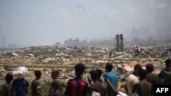 Палестинци наблюдават как палети с хуманитарна помощ се спускат с парашути, след като са били хвърлени от военен самолет над Нусейрат в централната част на ивицата Газа, 5 август 2025 г. 