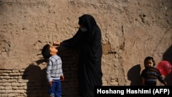 Egy burkás egészségügyi dolgozó polio elleni oltást csöpögtet egy gyerek szájába egy oltási kampány során Herát városában, Afganisztánban, 2020. október 27-én.