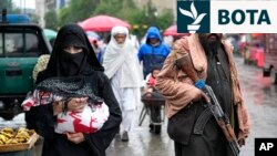 Një grua afgane duke ecur në një treg të vjetër të Kabulit, teksa afër i qëndron një luftëtar taliban.