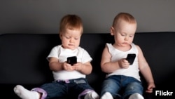 Dy fëmijë me telefona në duar.