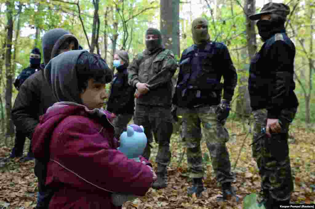 Egy iraki gyermeket és társait veszik körbe a lengyel határőrök és rendőrök a belarusz&ndash;lengyel határon található erdőben október 14-én