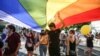 Mai multe persoane trec pe sub steagul curcubeu, simbolul LGBT, în timpul Marșului Diversității.