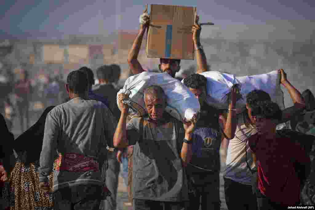 Burra e fëmijë palestinezë duke bartur thasë dhe pako me ndihma.