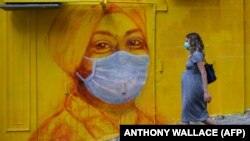Një grua shtatzënë e veshur me maskë ecën pranë një murale në Hong Kong, më 23 mars 2020. 