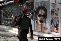 Talibanski borac prolazi pored kozmetičkog salona sa slikom žene nasprejane crnim sprejom, u Shar-e Nawu u Kabulu, 18. avgusta 2021.