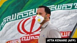 Мужчина в маске на фоне изображения государственного флага Ирана. Тегеран, 4 марта 2020 года.