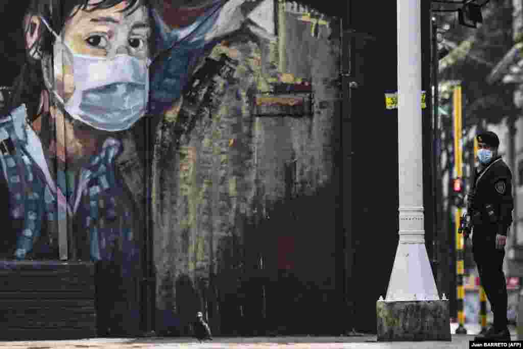 Полициски службеник во Колумбија стои пред мурал во Богота на 21 март.