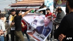 Protestatari distrugând un banner cu imaginea fostului președinte sirian, Bashar al-Assad, care a părăsit țara la 8 decembrie, după ce rebelii au pus stăpânire pe capitala Damasc.