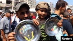 Un bărbat palestinian și un copil țin în mâini farfurii cu inscripțiile „Gaza este a noastră” și „Rezistență” la o manifestație pentru încetarea războiului din Gaza și împotriva strămutării, în orașul Gaza, 21 august 2025.