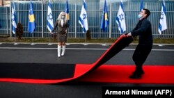 Косовски работник го влече црвениот тепих покрај знамињата на Косово и Израел, изложени за време на церемонијата во седиштето на Министерството за надворешни работи во Приштина, 1 февруари 2021 година