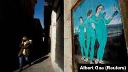 Жена с предпазна маска минава по улица в Барселона, Испания, на 27 януари 2021 г. На стената е залепена реклама на ваксините на Пфайзер, Модерна и АстраЗенека.