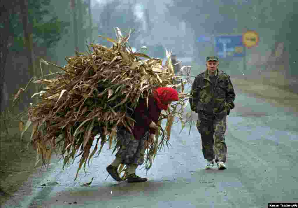 Bosanka nosi kukuruz, a pored nje prolazi vojnik u blizini nekadašnje prve linije u selu Lopare, u blizini Tuzle, 20. januar 1996. godine