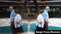 Stariji par nosi zaštitne maske za lice i ogleda se u čaši dok šetaju naseljem Usera za vrijeme djelimičnog zaključavanja u Španiji