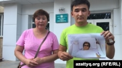 Житель Уральска Азамат Нурумов (справа) с фотографией своей матери стоит у здания областного управления здравоохранения, требуя привлечь к ответу врачей, которые, по его словам, отнеслись к работе халатно. Уральск, 14 июля 2015 года.