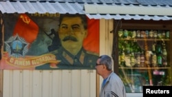 Мъж минава покрай билборд, от който се честити Деня на победата с лика на Сталин и силует на съветския войник, издигащ съветското знаме над Райхстага през 1945 г. Дебалцеве (Дебалцево), Донецка област, окупирана Украйна, 4 май 2025 г.