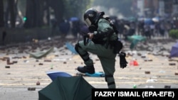 Pripadnik interventne policije gazi kišobran kojeg su koristili demonstranti tokom prodemokratskih protesta ispred univerziteta u Hong Kongu, novembar 2019.