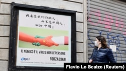Žena prolazi pored plakata u Milanu sa rukama u bojama kineske i italijanske zastave na kojem piše "Neprijatelj je virus, ne narod. Napred, Kina" 10. marta 2020. godine