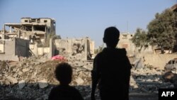 Copii se uită la distrugerile produse în urma unui atac israelian în tabăra de refugiați Nuseirat din centrul Fâșiei Gaza, la 7 noiembrie 2024, pe fondul războiului în curs dintre Israel și militanții palestinieni Hamas. (Foto: Eyad BABA / AFP)