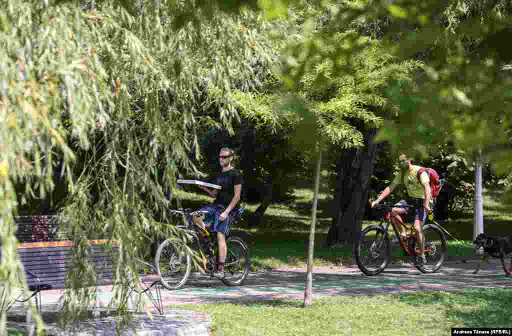 Doi bărbați se plimbă pe biciclete în Parcul Alexandru Ioan Cuza din București.