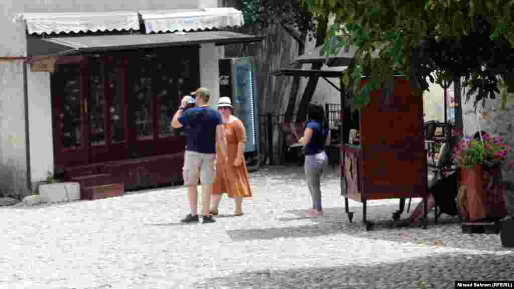 Turista u mostarskom Starom gradu pije vodu usred velike vrućine oko 13 sati, poštujući i preporuku da se na vrijeme boravka na otvorenom nose kape ili šeširi kao zaštita od sunca.