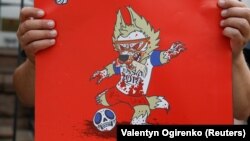 Demonstrant ispred ruske ambasade u Kijevu zahteva slobodu za Olega Sencova i drži poster protiv Rusije i Svetskog prvenstva