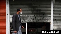 An Afghan man wearing a face mask walks by a damaged shop after a bomb explosion in Kabul on March 30.