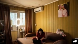 Olga kijevi lakásának nappalijában dolgozik a laptopján, mögötte egy kép róla és férjéről