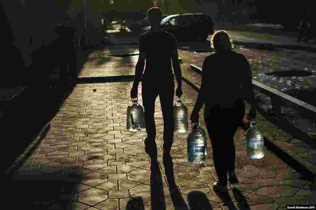 Брачен пар носи шишиња со вода откако ги наполни во продавница во Покровск на 4 август. Многу делови од регионот Доњецк се без редовно снабдување со вода.