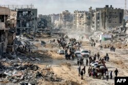 Oamenii trec pe lângă dărâmăturile clădirilor prăbușite de-a lungul străzii Saftawi din Jabalia, în nordul Fâșiei Gaza, pe 20 ianuarie 2025, la o zi după intrarea în vigoare a unui acord de încetare a focului în războiul dintre Israel și Hamas.