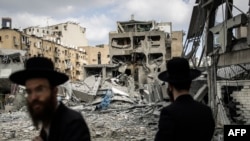 Ултраортодоксни Евреи ги проверуваат штетите на местото на иранскиот ракетен напад во Бнеи Брак, источно од Тел Авив, 16 јуни 2025 година