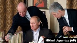 Пригожин (лево) и тогашниот руски премиер Владимир Путин (во средината) за време на вечерата со странски научници и новинари надвор од Москва во ноември 2011 година.