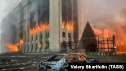 Сгоревшая машина на фоне охваченного огнем акимата Алматы в день, когда протесты вылились в беспорядки. 5 января 2022 года