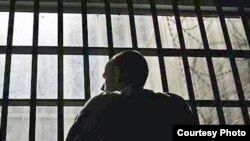 Человек смотрит из окна с решеткой. Иллюстративное фото. 