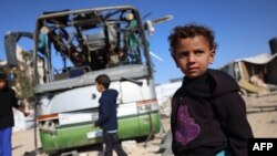 Mai mulți copii se uită la carcasa unui autobuz distrus de un atac israelian în zona Mawasi, la vest de orașul Khan Yunis, în sudul Fâșiei Gaza, pe 23 decembrie 2024.