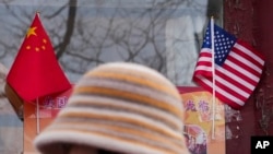 Një grua ec pranë flamurit kinez dhe atij amerikan, të ekspozuar pranë një dyqani në Pekin, më 31 janar 2025.