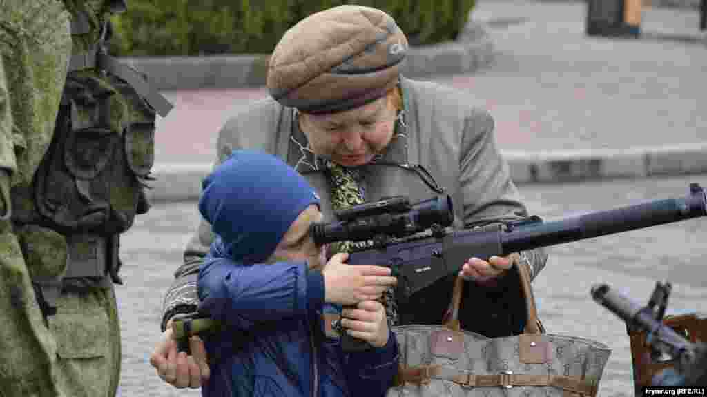 A woman helps a child aim a weapon during an exhibition of Russian military equipment in Sevastopol on April 12.&nbsp;